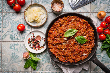 classic italian bolognese sauce stewed in a pan with ingredients on tile background, top view