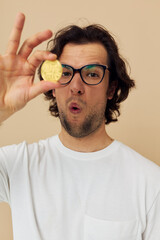 Cheerful man with glasses gold bitcoin in hands beige background