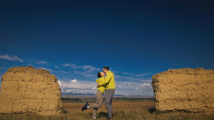 Man and woman in yellow green sportswear. Lovely couple of travelers hug and kiss near old stone enjoying highland landscape.