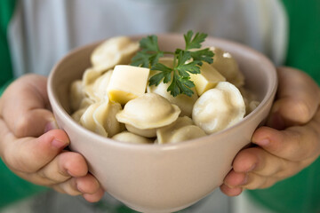 Boiled meat dumplings in bowl in child hand. Close-up view of russian boiled pelmeni on white plate. Boiled prepared homemade russian dumplings or pelmeni with beef meat.