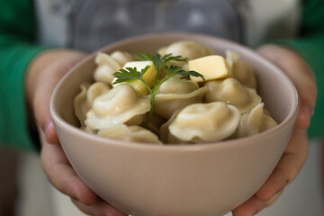 Boiled meat dumplings in bowl in child hand. Close-up view of russian boiled pelmeni on white plate. Boiled prepared homemade russian dumplings or pelmeni with beef meat.