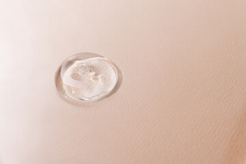 A drop of a cosmetic product on a beige texture background close-up, copy space. Transparent hyaluronic acid for skin care, top view.