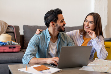 Obraz premium Loving couple using laptop and searching best tour, packing suitcases and preparing for long-awaited vacation