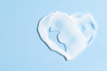 Smear of cream in the shape of a heart on a blue background with copy space. Beauty concept.