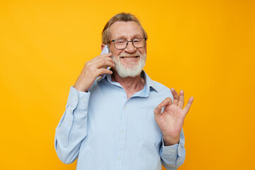 Senior grey-haired man talking on the phone posing close-up yellow background