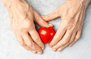Taking care for the elderly concept with a wrinkled hands holding red heart symbol.