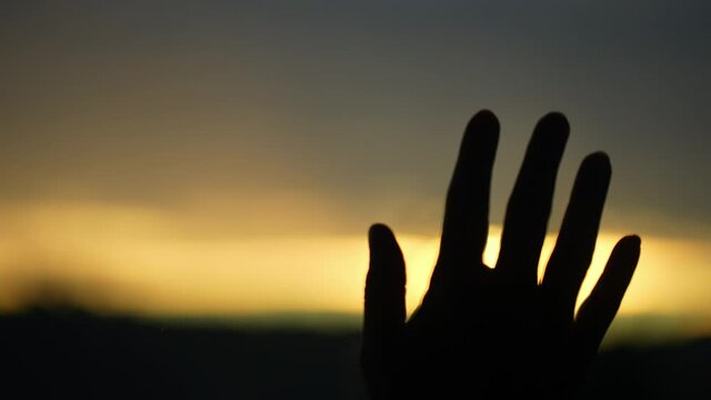 Woman's hand on the right side of the glass of a window covering the orange sun of the sunset or sunset.
