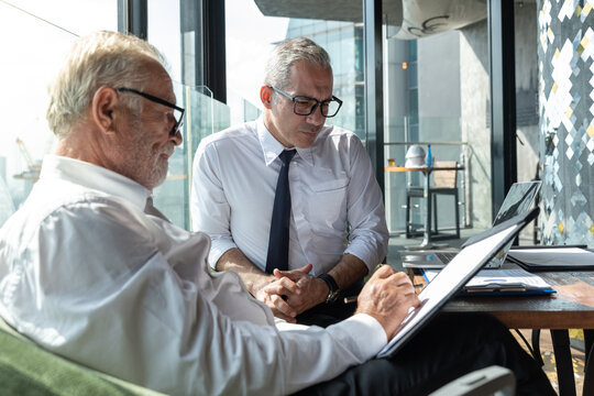Two business partner discuss their business plan with each other. They have their favorite drink with them. They are in a hotel lobby with beautiful cityscape scene behind them.