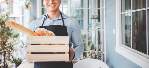 Male bakery business owner holding bread product bucket smiling at coffee shop, Entrepreneur business reopening concept