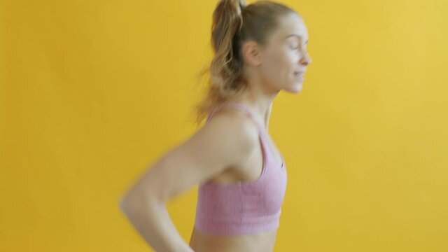 Side view of young sportswoman jogging then turning to camera and smiling on yellow background. People and active lifestyle concept.
