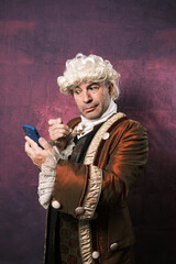 Man in classic renaissance clothes using an old monocle to see the mobile phone screen.