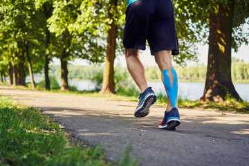 Man with kinesiology tape running in park during sunny summer day
