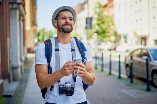 Smiling Young Tourist With Camera Using Phone During Holiday City Break