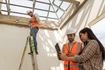 male engineer wearing a ladder gun uniform and a female employee and a male Foreman wearing a safety engineer's helmet discuss the installation of solar cells for renewable energy. 