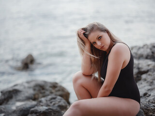 Portrait of attractive blonde woman with long hair posing on rocky beach.