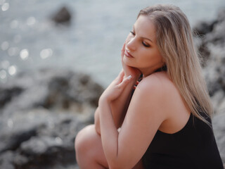 Portrait of attractive blonde woman with long hair posing on rocky beach.