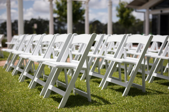 Rows white timber wedding chairs outdoors grass bright sunny day celebratrion happy gathering together love happy