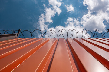 Orange corrugated metal panels, aluminium fence with barbed wire securing a warehouse.