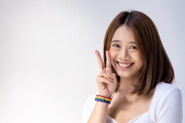 Happy LGBT woman wearing LGBTQ rainbow wristband, showing V sign for Victory of LGBT awareness, concept of gay pride month, non-binary inclusivity and diversity