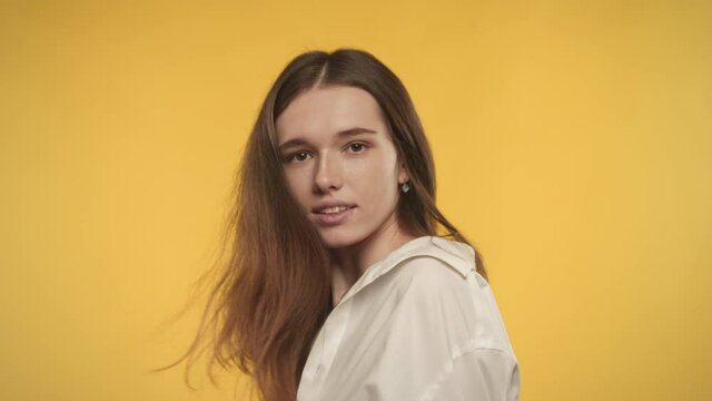 Young adult caucasian woman is turning and shaking her hair on a bright yellow background