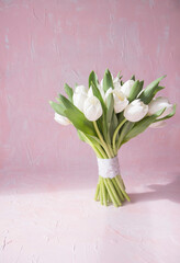 White tulips bouquet flowers and ray of light on vintage pink background. Front view with copy space. Studio shot photo.