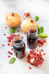 Healthy juicy vitamin drink diet or vegetarian food concept. Pomegranate juice in glass bottles with pomegranates on a light stone tabletop.