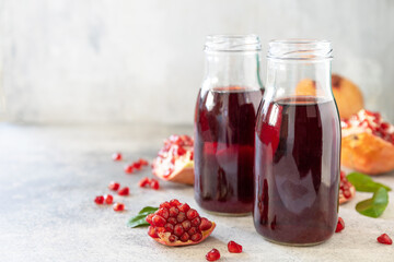 Healthy juicy vitamin drink diet or vegetarian food concept. Pomegranate juice in glass bottles with pomegranates on a light stone tabletop. Copy space.