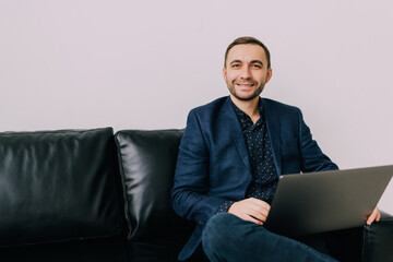 Young business man working on laptop sittingon sofa at home. Remote job.