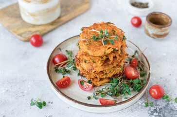 Crispy sweet potato fritters served with tomatoes and green sprouts on ceramic plate. Healthy vegan diet food. closeup