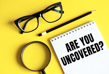ARE YOU UNCOVERED written on a notebook with glasses, magnifying glass and pencil