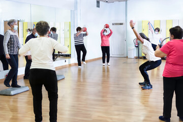 Group of women retired seniors attending gym class. Wearing protective mask, social distancing. Concept of active, wellness retirement.