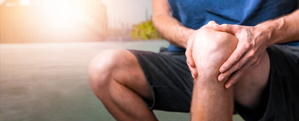 Young man suffering from knee pain during run jogging, close up with sport blurred background....