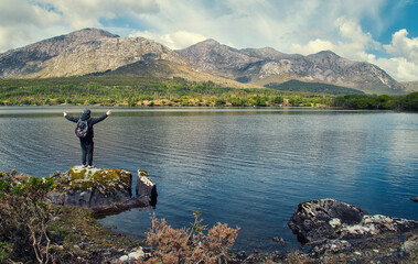 Fototapeta na wymiar Person standing on the rock by the lough inagh with mountains in the background at Connemara National park in county Galway, Ireland 