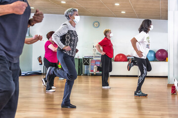 Group of women retired seniors attending gym class. Wearing protective mask, social distancing,...