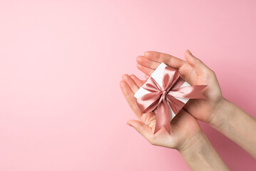 First person top view photo of saint valentine's day decorations young woman's hands giving small white giftbox with pink ribbon bow on isolated pastel pink background with copyspace