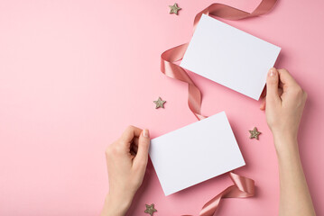 Obraz premium First person top view photo of valentine's day decorations woman's hands holding two paper sheets shiny stars and satin curly ribbon on isolated pastel pink background with blank space