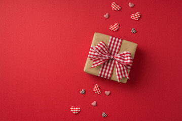 Top view photo of valentine's day decorations craft paper giftbox with checkered ribbon bow and hearts on isolated red background with empty space