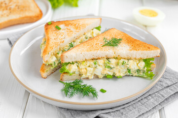 Egg salad sandwich with toasted bread and lettuce on a white wooden background. Selective focus