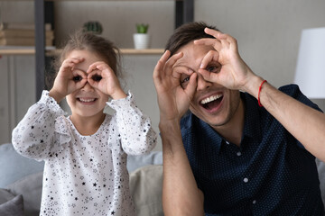 Cheerful cute small 6s kid girl making funny grimaces with caring loving single father, having fun together at home. Joyful bonding two generations family having fun, entertaining on weekend indoors.