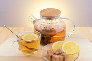 Herbal green tea in a glass teapot and a cup with lemon and brown sugar pieces.