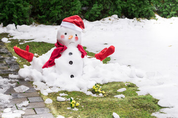 Unhappy snowman in mittens, red scarf and cap is melting  outdoors on snowy grass with yellow tiny...