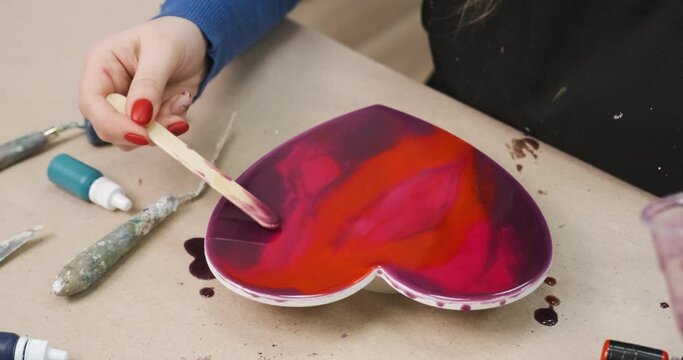 Making handmade gift for Saint Valentine's Day. Painting red heart with epoxy resin. Preparing for Valentine Day of all beloved, unrecognizable girl crafting the present for her boyfriend