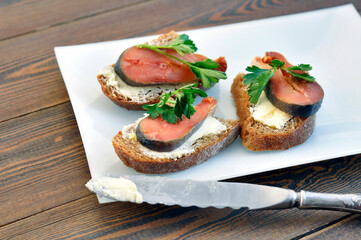 Salty fish. Pieces of bread with butter, salted salmon and parsley and a knife on a white rectangular dish