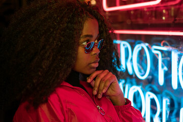 Millennial enigmatic pretty girl with unusual dyed hairstyle near glowing neon wall at night....