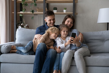 Happy relaxed sincere two generations family looking at cellphone screen, enjoying playing mobile games, watching funny photo video content online in social network, sitting on cozy couch at home.