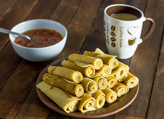 Russian pancakes on a brown dish and a dark wooden background close-up with a mug of tea and jam
