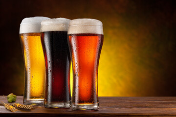 Cooled glasses of  three different beer on the wooden table. Dark brown background.