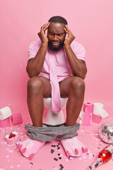 Dark skinned bearded man suffers from headache feels unwell has hangover after party poses on...