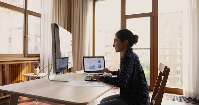 Indian female trader sit at desk analyze infographic diagram seen on pc monitor, make stocks data analysis of charts, graphs shown on computers. Sales, company growth, trading, cryptocurrency concept