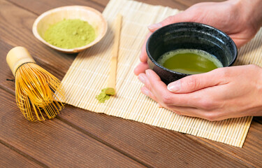 Girl's hands holding matcha tea in special traditional japanese matcha tea bowl with bamboo spoon...